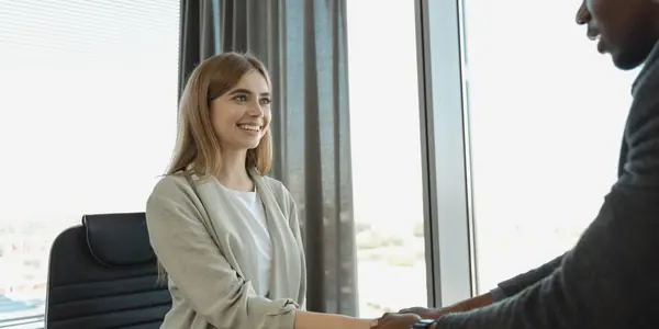 Aperto de mãos entre recrutadora e candidato ao fim de uma entrevista de emprego, cena que representa a contratação do primeiro funcionário e seus custos