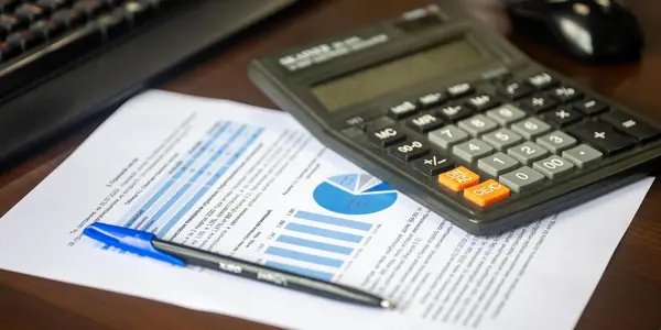 Calculadora, caneta e relatório contábil com gráficos sobre mesa de madeira, usados para calcular a distribuição de lucros isenta de uma empresa