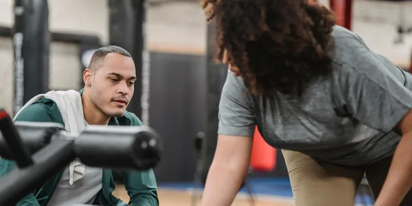Personal trainer orientando uma aluna durante um exercício em um aparelho de academia.
