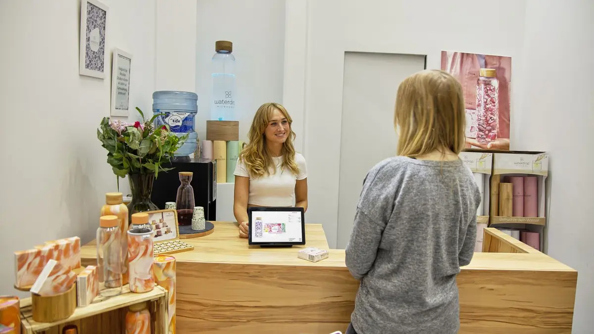 Recepção de clínica de estética com balcão de madeira, atendente e cliente.