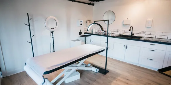 Sala de clínica de estética com maca, luminária circular e bancada branca.