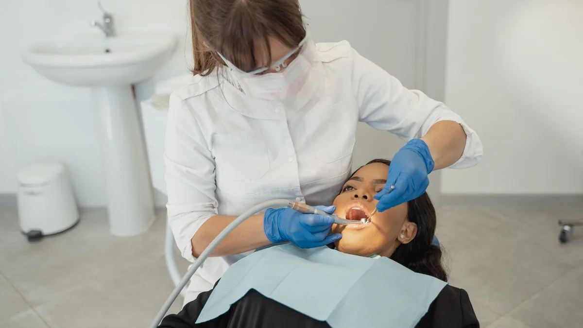 Dentista atendendo uma paciente na cadeira do consultório, em sala clara.