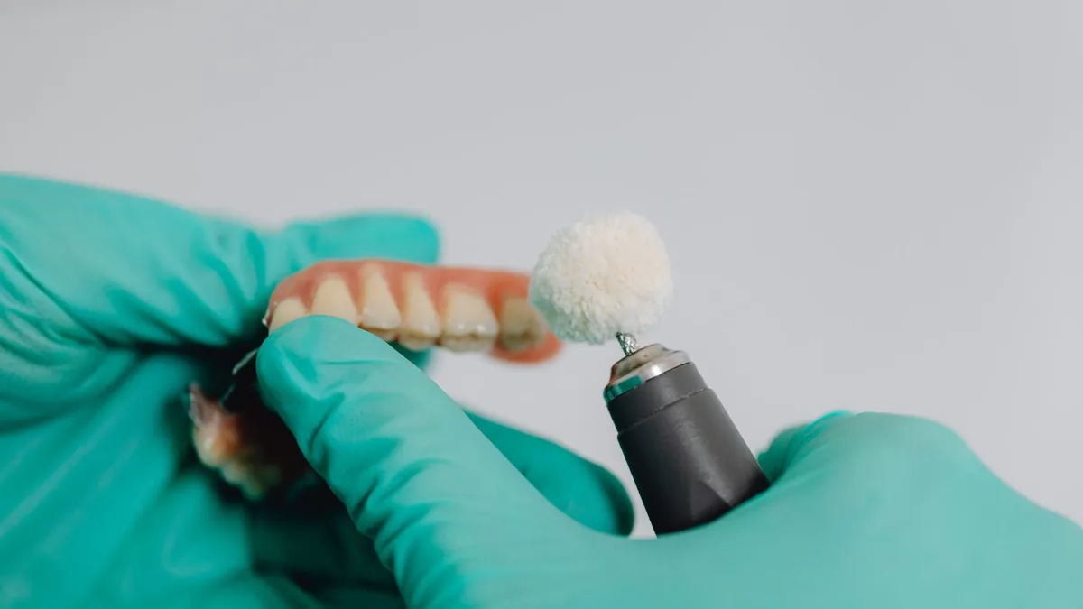 Técnico com luvas polindo uma prótese dentária em laboratório.