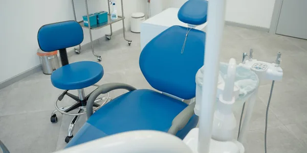 Cadeira de consultório odontológico com refletor e equipamento ao lado.