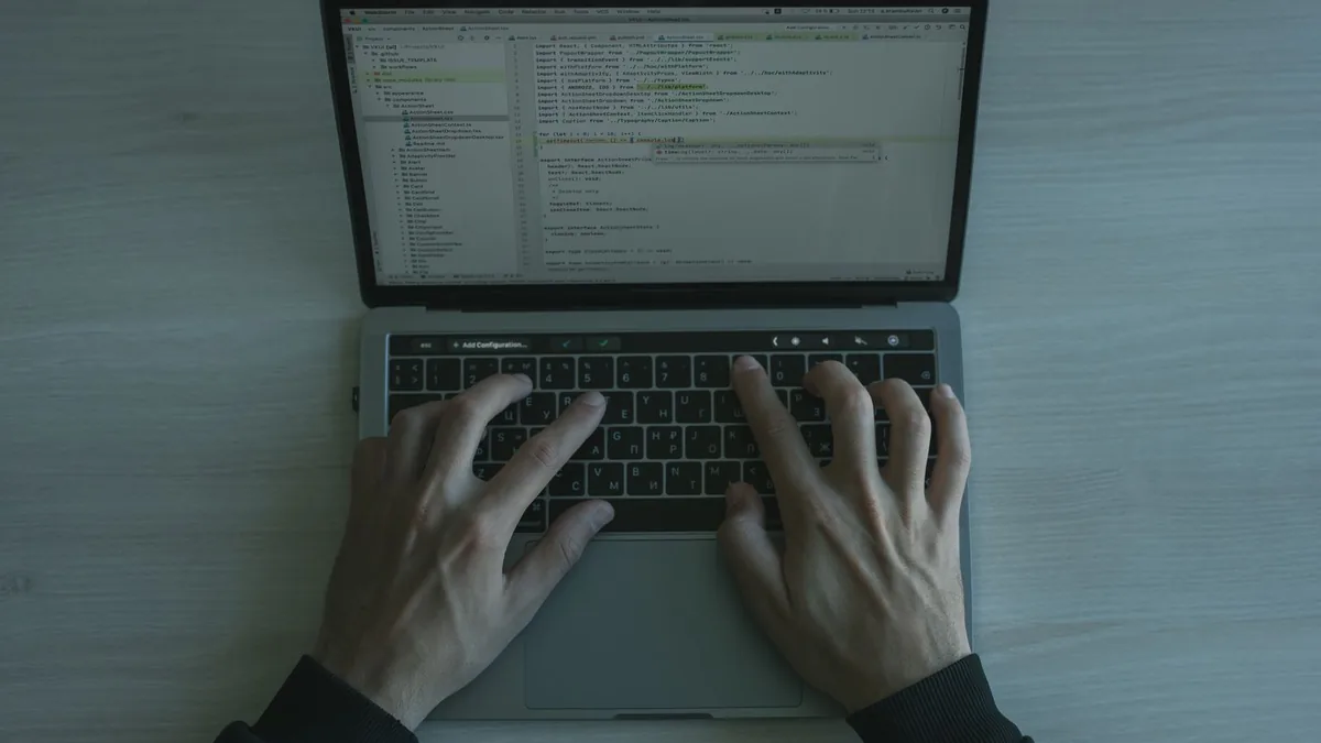 Mãos digitando em um notebook com código na tela, vistas de cima.