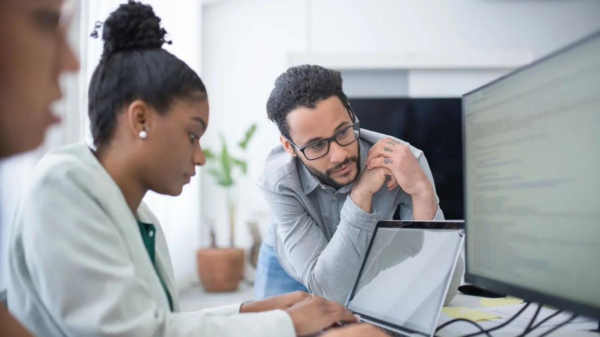 Duas pessoas revisando o conteúdo de um monitor durante uma reunião de trabalho.