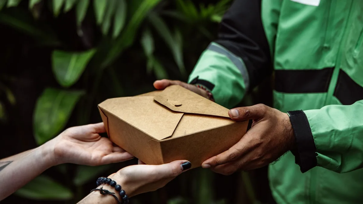 Entregador passando uma embalagem de papelão às mãos de um cliente.