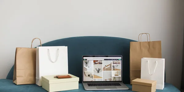 Sacolas de compras e caixas ao lado de um notebook aberto sobre o sofá.