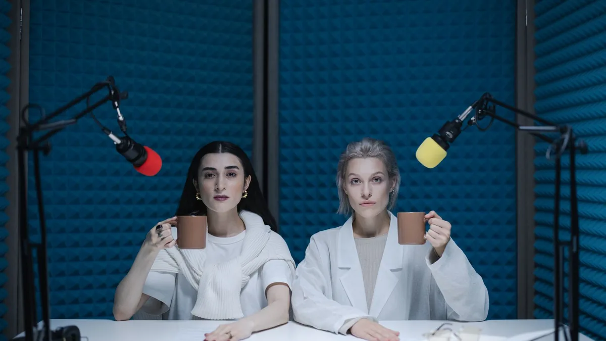 Duas pessoas sentadas diante de microfones durante a gravação de um podcast.