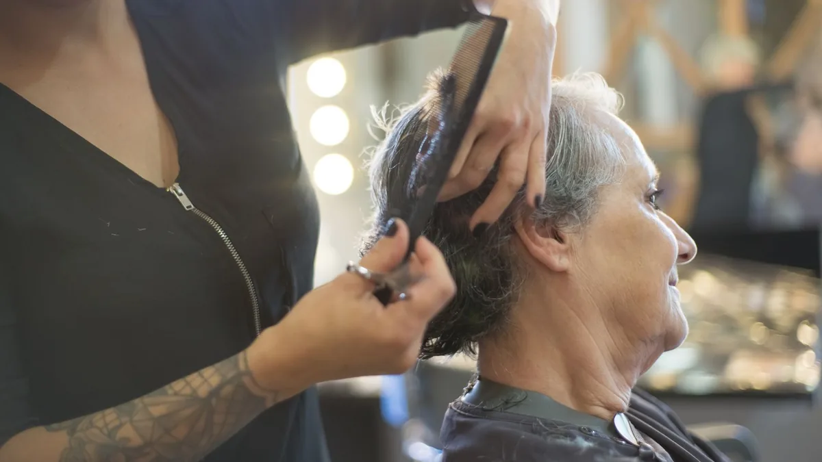 Cabeleireiro penteando o cabelo de uma cliente sentada na cadeira do salão.