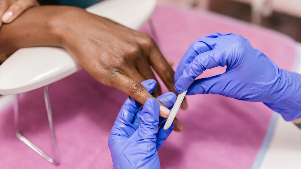 Manicure com luvas fazendo as unhas de uma cliente sobre a toalha rosa.