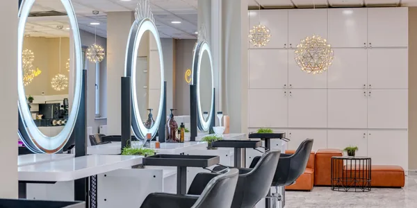 Interior de salão de beleza com espelhos iluminados e cadeiras alinhadas.