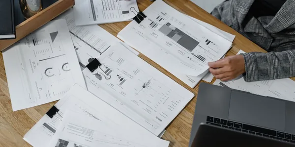 Mulher analisando relatórios financeiros em uma mesa de madeira com notebook