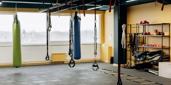 Interior vazio de um box de treinamento funcional, com sacos de pancada pendurados, argolas e prateleira de equipamentos.