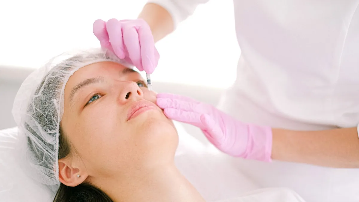 Esteticista realizando procedimento facial em cliente deitada na maca da clínica