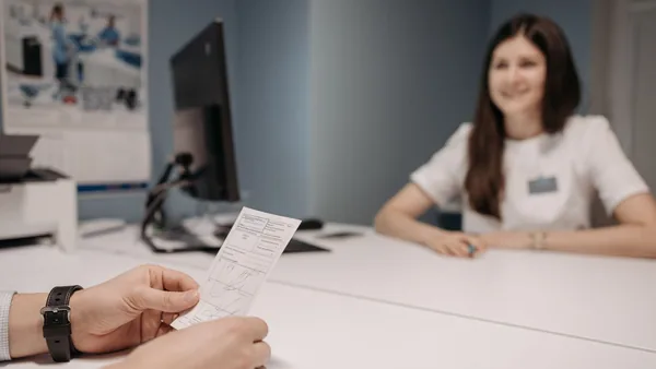Atendimento na mesa de uma clínica médica, com o paciente conferindo um comprovante