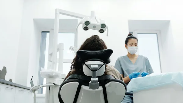 Dentista e auxiliar atendendo um paciente na cadeira do consultório odontológico