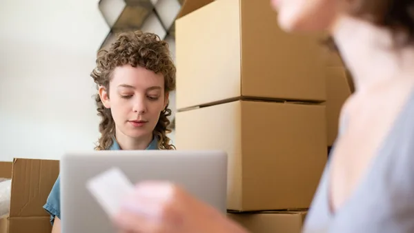 Empreendedora conferindo pedidos no notebook em meio às caixas da loja virtual