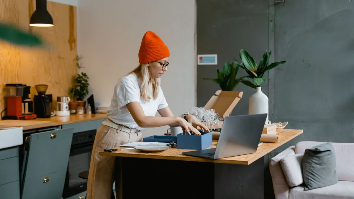 Empreendedora conferindo os pedidos no notebook, ao lado das caixas de envio