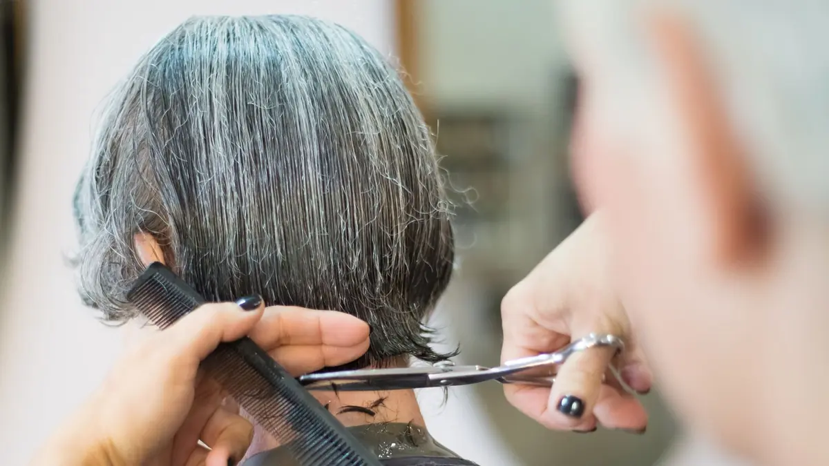 Cabeleireira finalizando o corte de uma cliente na cadeira do salão