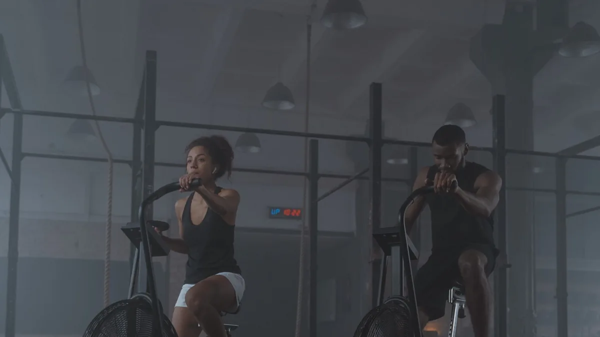 Dois alunos treinando em bicicletas de ar no salão da academia