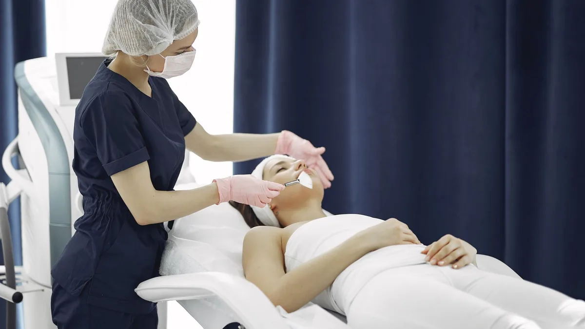 Esteticista aplicando um tratamento facial em uma cliente na maca