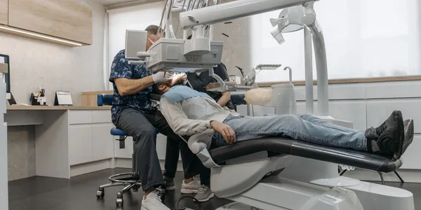 Dentista atendendo um paciente com os equipamentos da cadeira odontológica