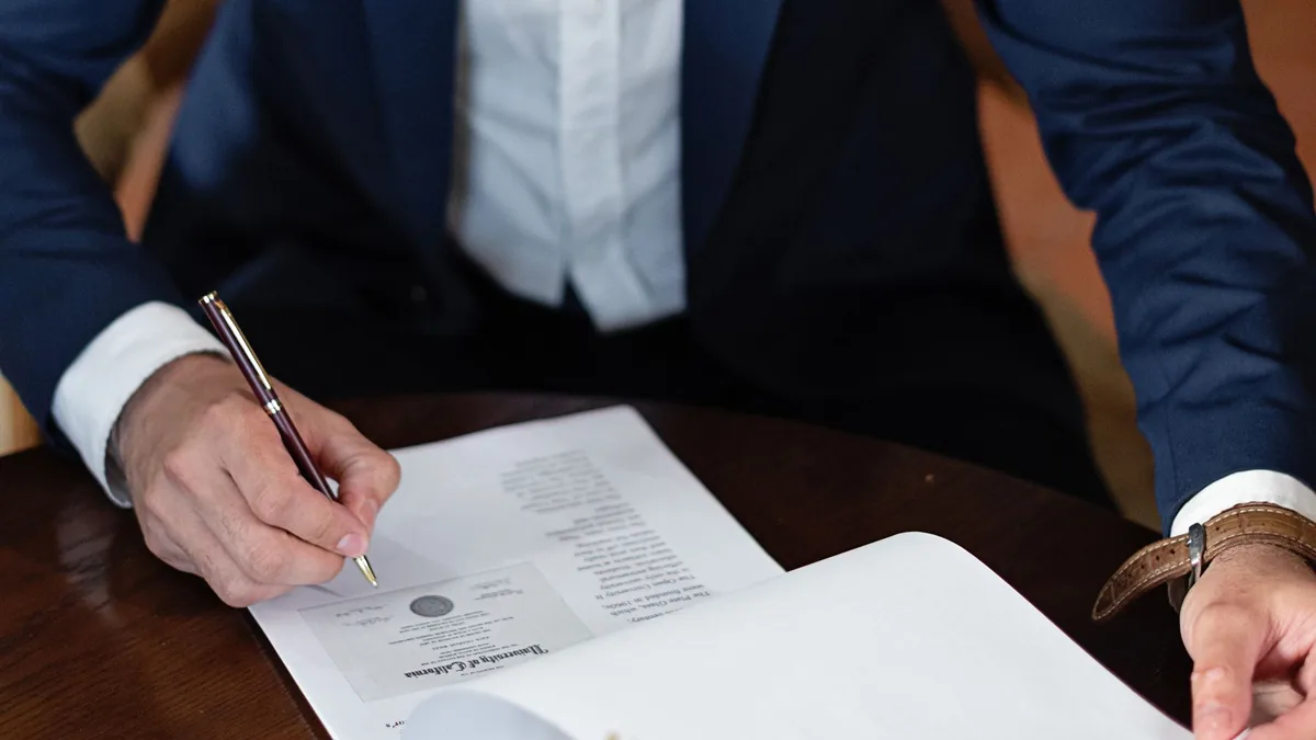 Profissional de terno assinando documentos na mesa do escritório