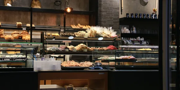 Balcão de padaria com vitrines refrigeradas cheias de pães, salgados e doces.