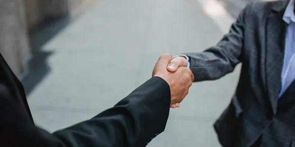 Aperto de mãos entre dois profissionais de terno ao fechar um pedido.