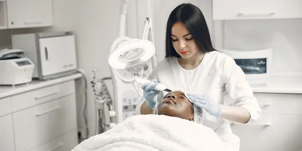 Esteticista aplicando tratamento facial em uma cliente na maca da clínica, cena típica do salão de beleza e estética