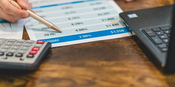 Mão com caneta conferindo números em relatório fiscal ao lado de notebook, representando a correção de rejeições da nota fiscal