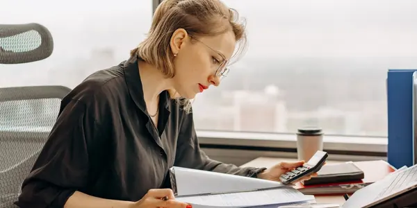 Contadora sentada à mesa do escritório conferindo documentos com a calculadora na mão, rotina de quem acompanha as mudanças do Simples Nacional