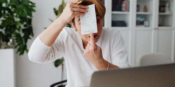 Profissional autônoma na mesa de trabalho com notebook, calculadora e papéis, fazendo contas para decidir se vale a pena abrir empresa para emitir nota fiscal